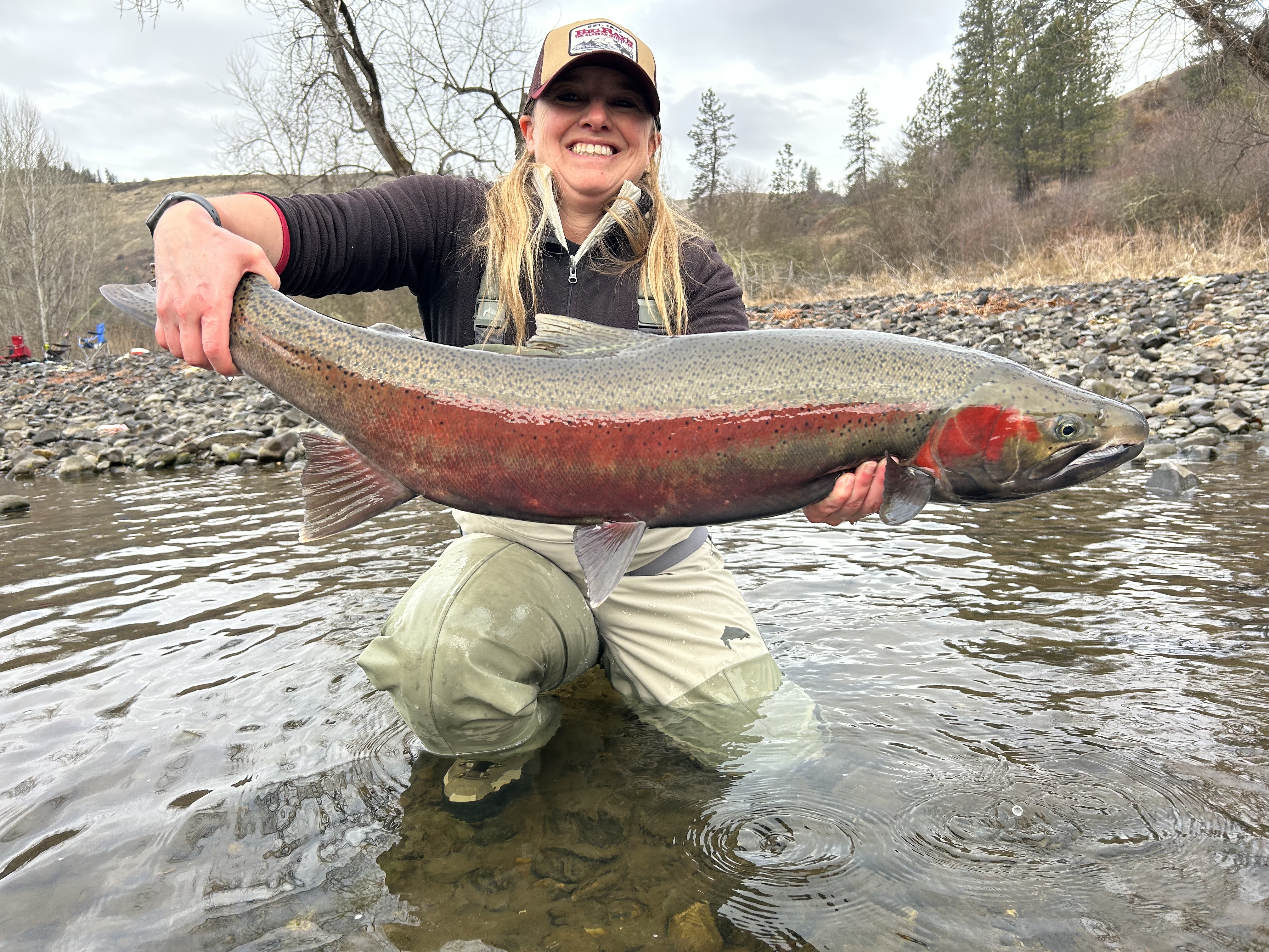 Female angler crouches down while holding a large steelhead